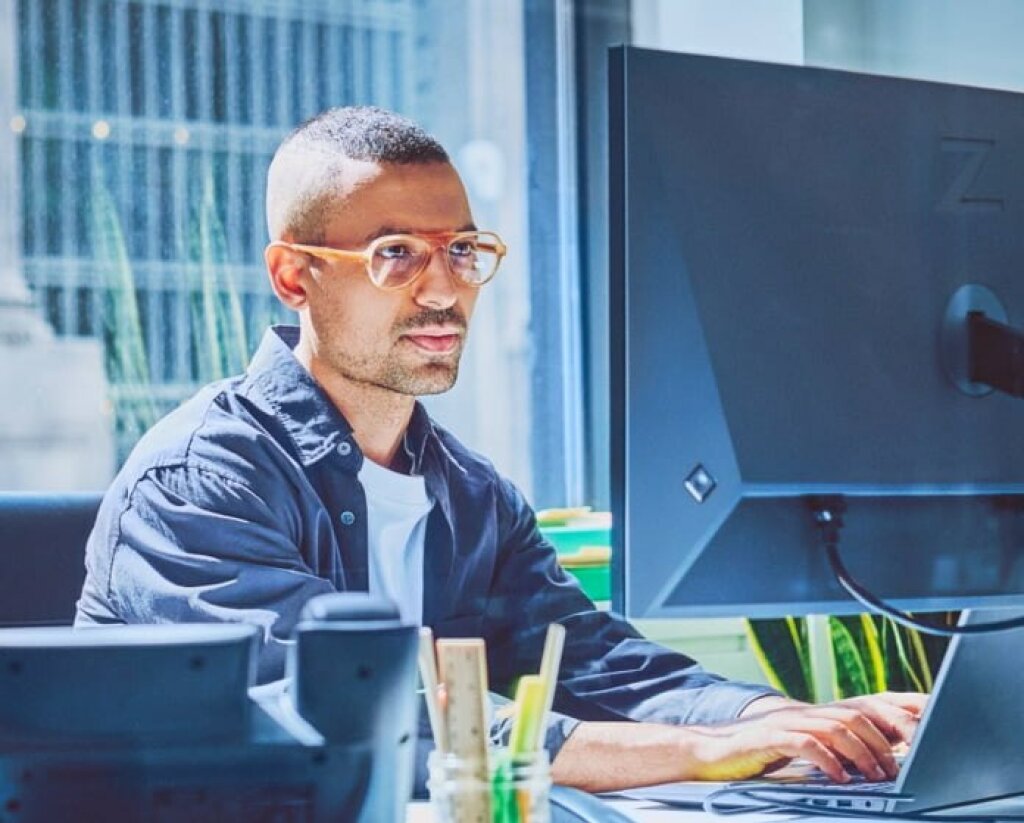 Auf dem Bild sieht man ein Mann, welcher vor einem HP Monitor sitzt und Rechner was tippt.