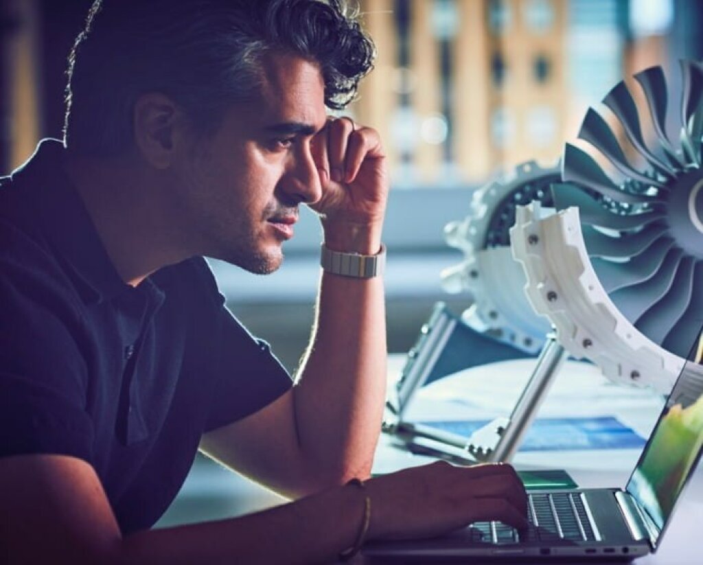 Auf dem Bild sieht man ein Mann, der vor einem Rechner sitzt und was konstruiert.